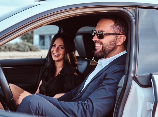 Well-dressed couple - smiling bearded male and beautiful woman sitting on the front seats in a luxury car.