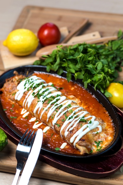 Free photo wet burrito in tomato sauce garnished with cream