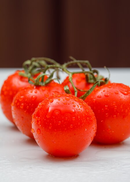 Wet fresh tomatoes side view on a white surface