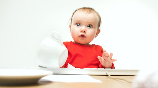 What Surprised child baby girl sitting with keyboard of modern computer or laptop in white studio