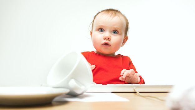 What Surprised child baby girl sitting with keyboard of modern computer or laptop in white