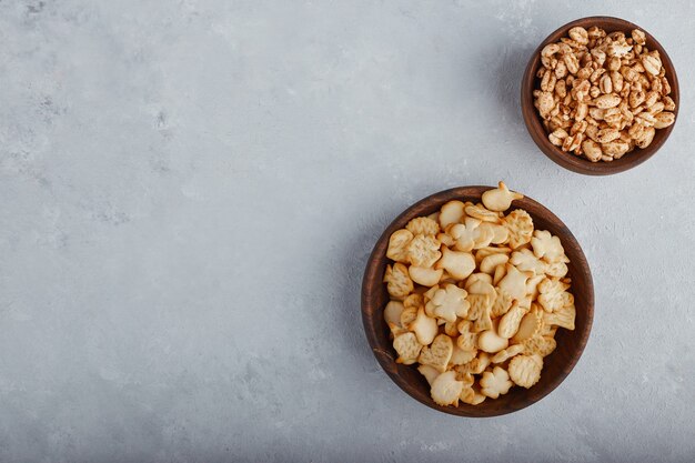 Wheat popcorns and crackers in a wooden bowl on stone surface, top view. 