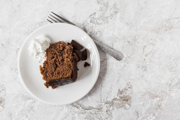 Whipped cream and slice of cake on plate with fork over the marble counter