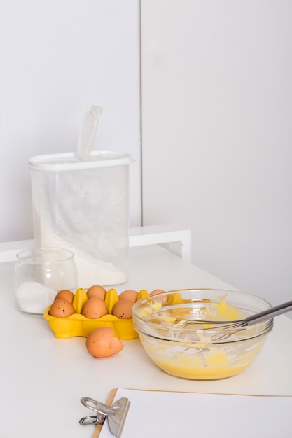 Free photo whipped eggs; egg carton; flour; salt and paper on clipboard on table