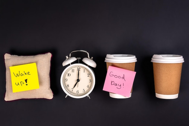 Free photo white alarm clock disposable cups and a small pillow on a dark background