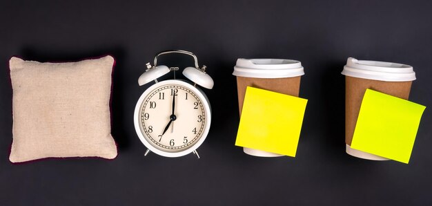 Free Photo white alarm clock disposable cups and a small pillow on a dark background