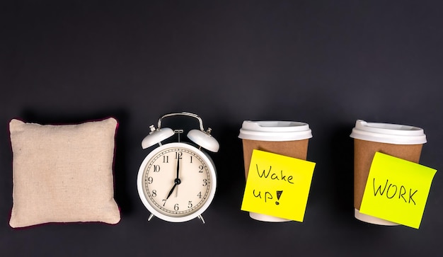 Free photo white alarm clock disposable cups and a small pillow on a dark background