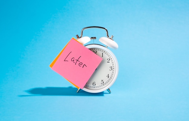 Free photo white alarm clock and sticker with the inscription late on a blue background