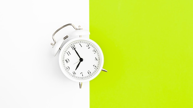 White alarm clock on a white and green background flat lay