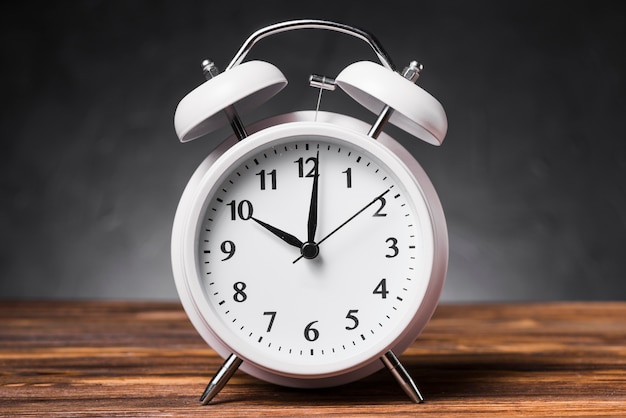 White alarm clock on wooden textured table showing 10'oclock