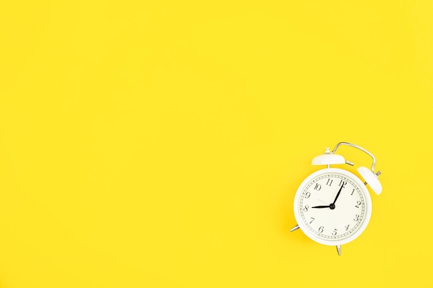 Free photo white alarm clock on a yellow background flat lay