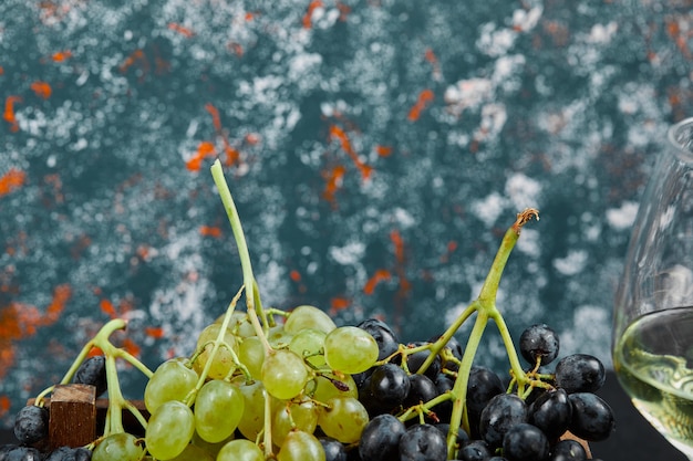 Free photo white and black grapes with a glass of wine on blue background. high quality photo