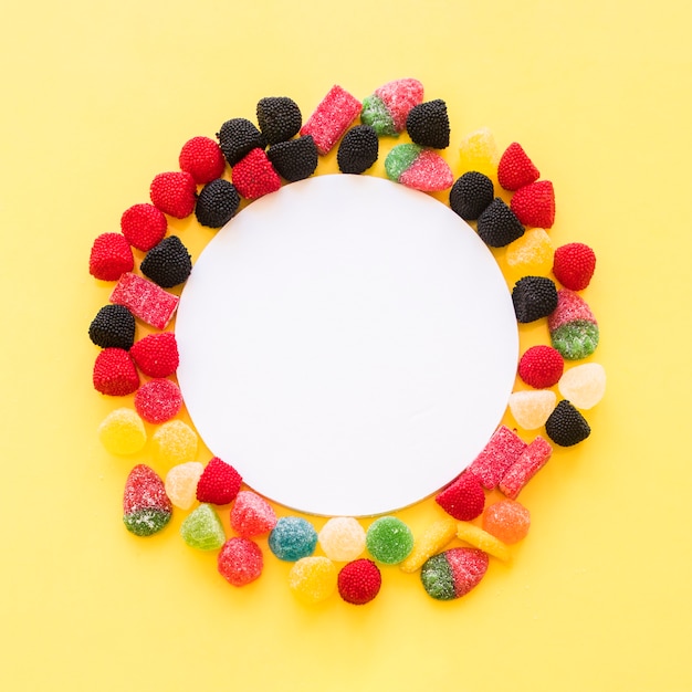 White blank frame surrounded with colorful jelly candies on yellow background