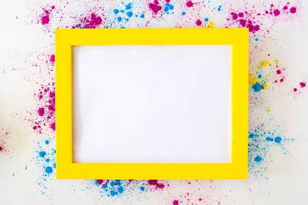 Free Photo white blank frame with yellow border on holi color powder over white background