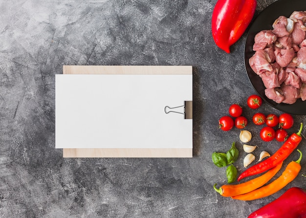 Free photo white blank paper on clipboard with ingredients for making meat on textured backdrop