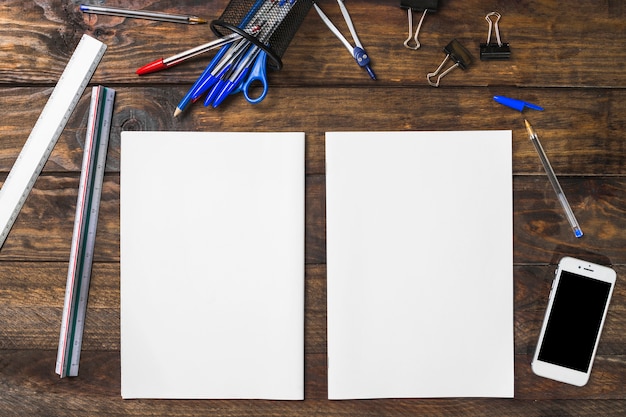 White blank paper surrounded with stationeries and smartphone on wooden table