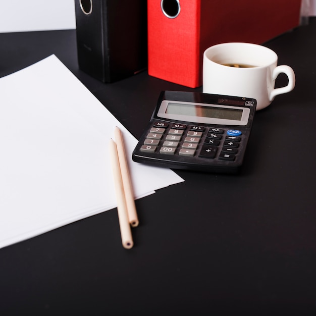 Free photo white blank papers; pencils; paper files; coffee cup and calculator on black desk