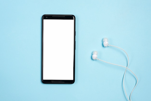 White blank screen display on mobile phone with earphones against blue background