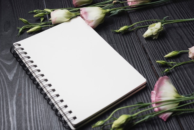 Free photo white blank spiral notepad with purple eustoma flowers over the wooden desk