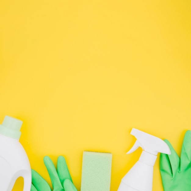 White bottles with green gloves and sponge on yellow backdrop