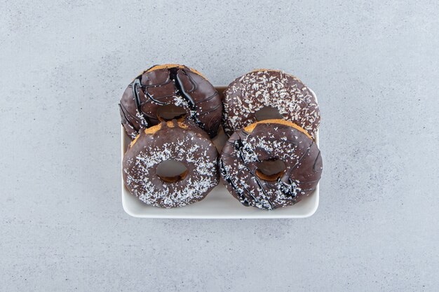 White bowl of four chocolate donuts on stone background. High quality photo