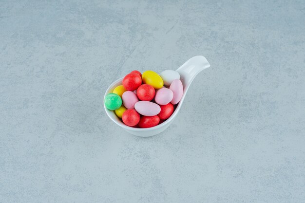 A white bowl full of round sweet colorful candies on white surface