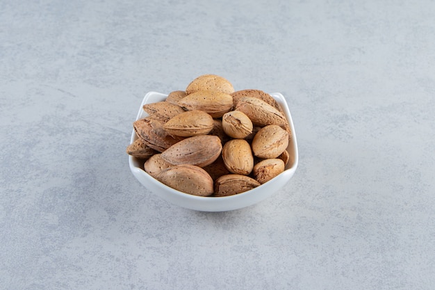 White bowl full of shelled almonds on stone background.