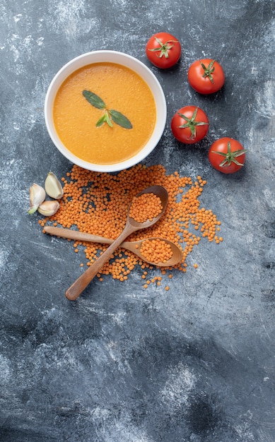 A white bowl of lentil soup with tomatoes and wooden spoons .