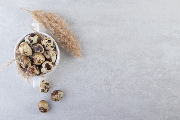 White bowl of raw quail eggs on stone table.