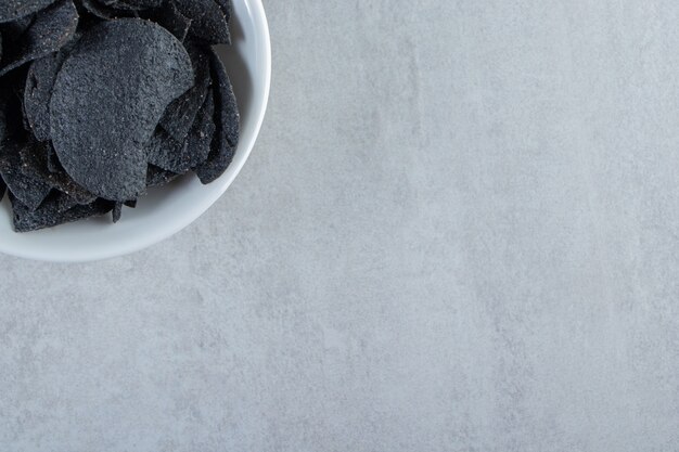 White bowl of salted crispy black chips on stone.