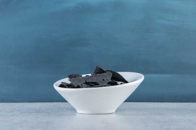 White bowl of salted crispy black chips on stone.