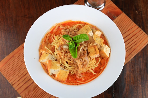 White bowl of soup with some spaghetti and bread pieces decorated with greens