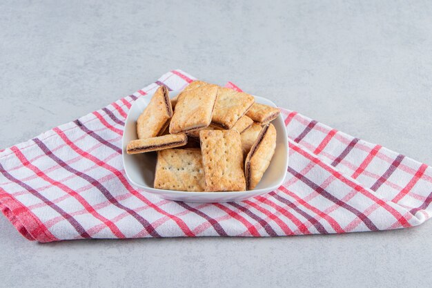 White bowl of tasty crispy crackers on stone background.