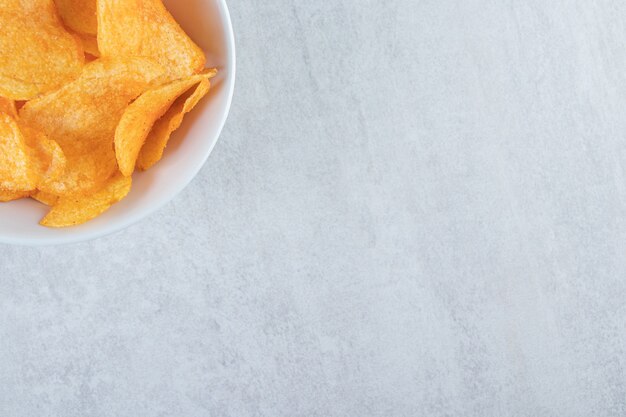 White bowl with delicious potato chips placed on stone.