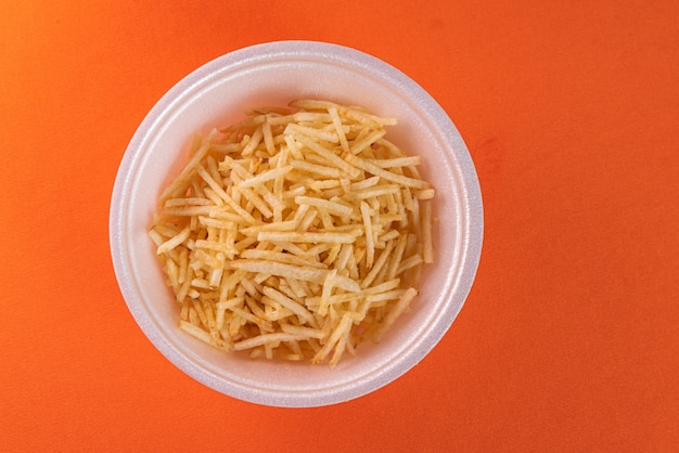 Free photo white bowl with potato straw on orange surface