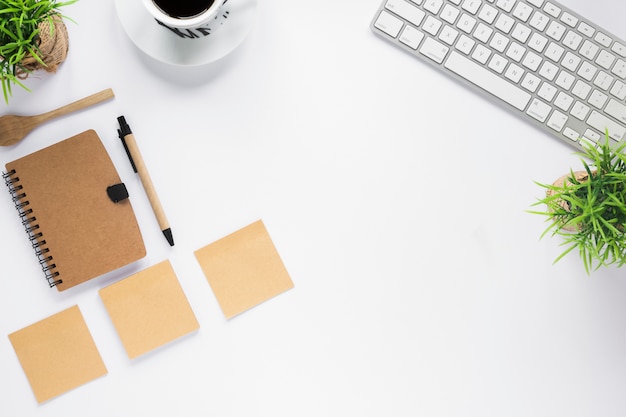 White business desk with diary; adhesive notes; coffee cup and keyboard on white desk