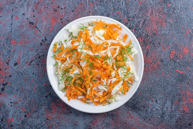 White cabbage and carrot salad on a platter on black table.