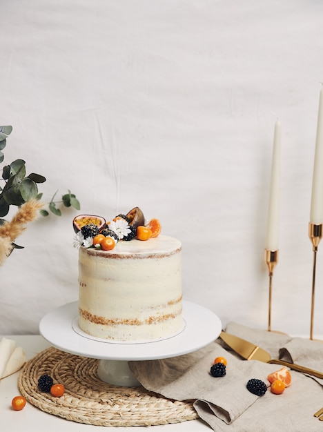 White cake with berries and passionfruits next to a plant behind a white