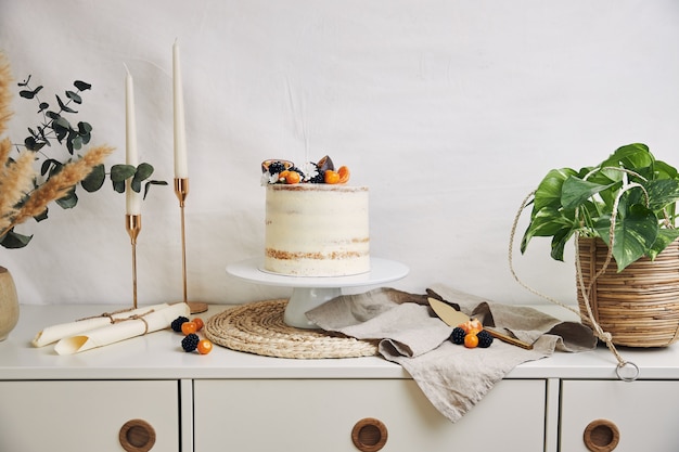 Free photo white cake with berries and passionfruits next to plants and candles on white