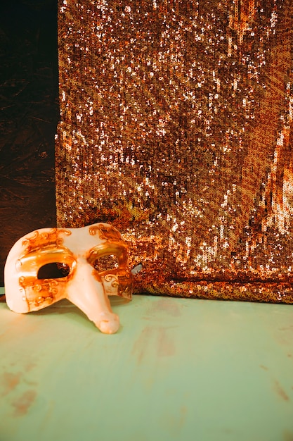 Free Photo white carnival mask near the glitter golden sequins textile on green weathered surface