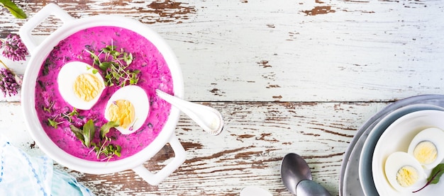 White casserole with cold summer beet cucumber and egg soup on a wooden table Top view