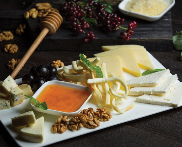 White ceramic cheese plate with different kinds of cheese, nuts and honey