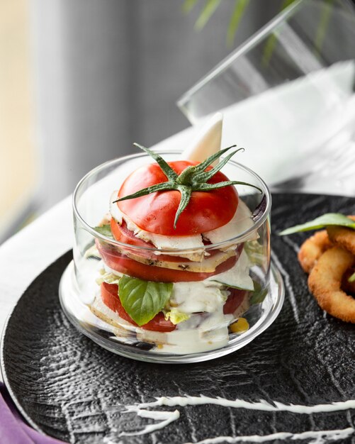 White cheese and tomato slices inside a glass with mint.