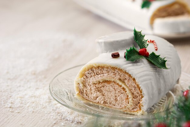 White chocolate yule log cake with christmas lights and ornaments on wooden table