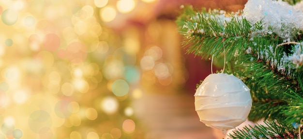 White Christmas ball hanging on a snowy fir tree branch, bokeh effect background