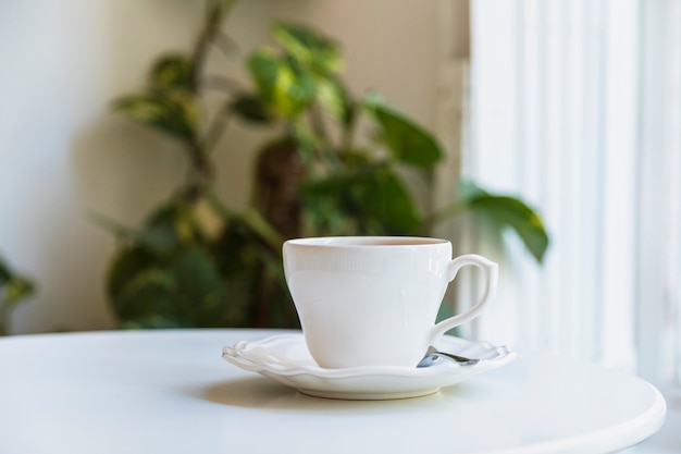 White coffee cup and spoon on ceramic saucer over white table