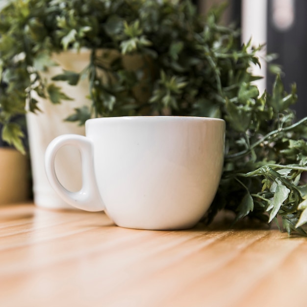 Free photo white coffee cup with potted plant on wooden desk