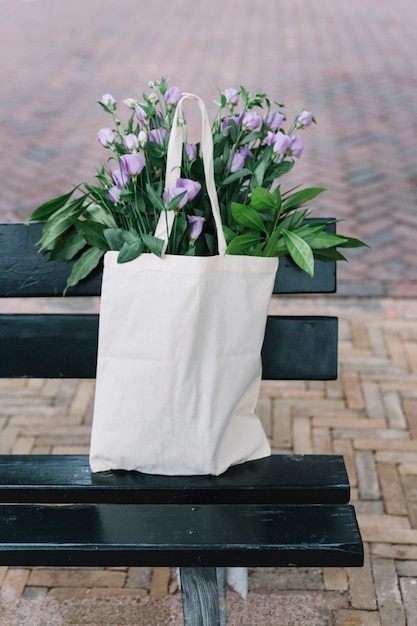 White cotton handbag with beautiful purple eustoma flowers in the black bench