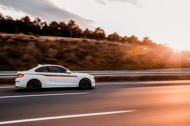 Free Photo white coupe sedan driving on the road in the sunset