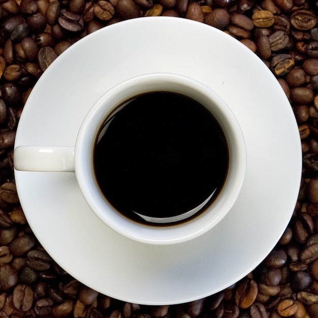 a white cup of black coffee on a surface full of coffee beans